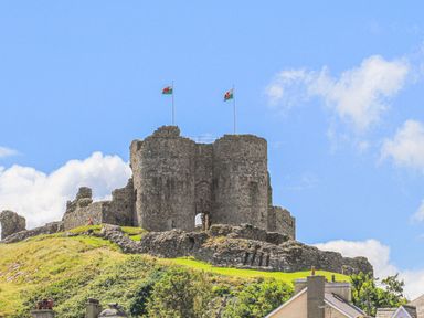 A stone castle ruin on a hill with two flags flying at Hafod Y Mor in Criccieth