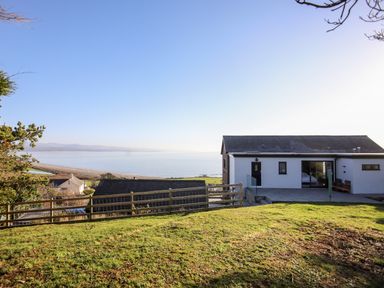 A house with a patio overlooking the sea and a grassy yard at Hafod Y Mor in Criccieth