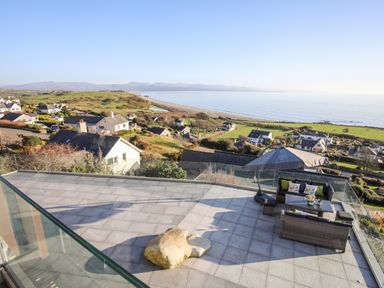 A patio with outdoor furniture and umbrella overlooking houses hills and the ocean at Hafod Y Mor in Criccieth