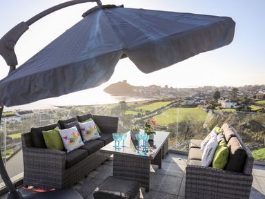 A rooftop patio with outdoor seating glass table and umbrella overlooking a coastal town at Hafod Y Mor in Criccieth