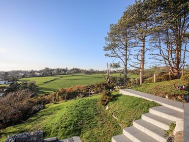 A garden with steps and trees overlooking fields and houses at Hafod Y Mor in Criccieth