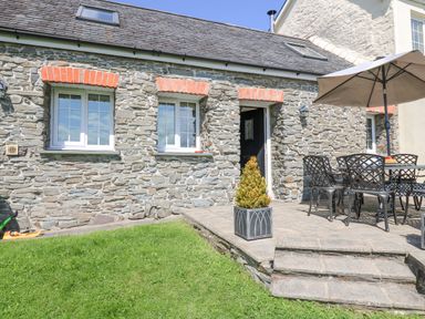 A stone house exterior with two windows a black door and outdoor seating with an umbrella at Yr Hen Beudy in Capel Bangor