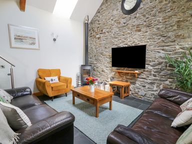A living room with two leather sofas a yellow armchair wooden tables a wall clock and a stone wall at Yr Hen Beudy in Capel Bangor