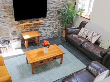 A living room with wooden tables leather sofas and a TV mounted on a stone wall at Yr Hen Beudy in Capel Bangor