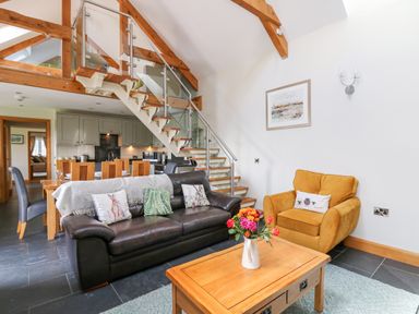 An open living room and kitchen area with a black leather sofa and a yellow armchair at Yr Hen Beudy in Capel Bangor