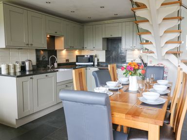 A kitchen and dining area with set table and flowers on table at Yr Hen Beudy in Capel Bangor