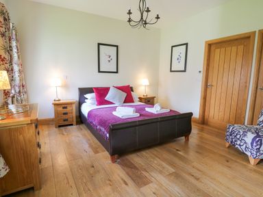 A bedroom with a bed two bedside tables wooden doors and an armchair at Yr Hen Beudy in Capel Bangor