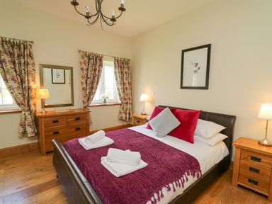 A bedroom with a bed covered with a purple throw and pillows and wooden furniture at Yr Hen Beudy in Capel Bangor