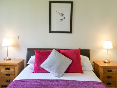 A bedroom with a bed with red and gray pillows and wooden nightstands with lamps at Yr Hen Beudy in Capel Bangor