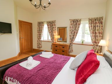 A bedroom with a bed red and grey pillows wooden dresser and floral curtains at Yr Hen Beudy in Capel Bangor