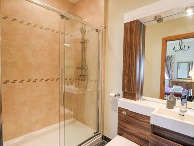 A bathroom with a glass shower enclosure and a sink with wooden cabinets at Yr Hen Beudy in Capel Bangor