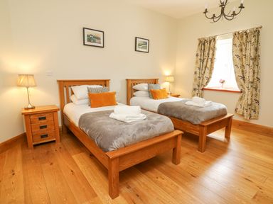 A bedroom with two single wooden beds bedside tables lamps and a window with floral curtains at Yr Hen Beudy Capel Bangor