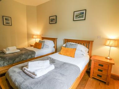 A bedroom with two single beds bedside tables with lamps and framed pictures on the wall at Yr Hen Beudy in Capel Bangor