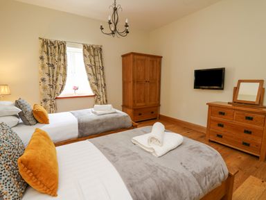 A bedroom with two single beds a wooden wardrobe and dresser and a wall-mounted TV at Yr Hen Beudy in Capel Bangor