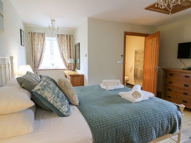 A bedroom with a made bed with folded towels a chest of drawers and an open door to a bathroom at Yr Hen Beudy in Capel Bangor