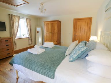 A bedroom with a bed covered in a blue quilt and pillows a wooden wardrobe and dresser and a standing mirror at Yr Hen Beudy in Capel Bangor