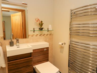 A bathroom with a rectangular sink wooden cabinets a mirror a glass shelf a toilet paper holder and a metal towel rack at Yr Hen Beudy in Capel Bangor