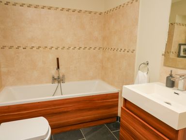 A bathroom with a bathtub a toilet and a sink with wood paneling at Yr Hen Beudy in Capel Bangor