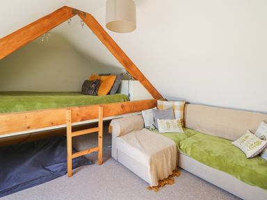 A bedroom with a wooden framed bed and a sofa with cushions and throws at Yr Hen Beudy in Capel Bangor
