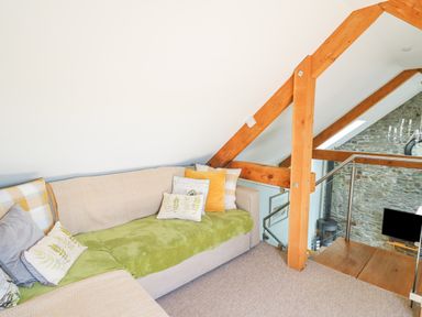A small seating area with a sofa and cushions near wooden beams and a glass railing at Yr Hen Beudy in Capel Bangor
