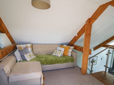 A seating area with a sofa covered with cushions and throws and wooden beams at Yr Hen Beudy in Capel Bangor