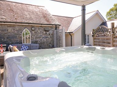 An outdoor jacuzzi with a stone wall and seating area with cushions at Yr Hen Beudy in Capel Bangor