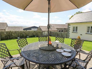 An outdoor patio with a round metal table and six chairs under a large umbrella at Yr Hen Beudy in Capel Bangor
