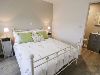 A bedroom with a white metal bed frame green pillows and two bedside tables with lamps at Cartref in Trawsfynydd