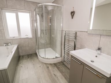 A bathroom with a bathtub shower cubicle sink and towel rack at Cartref in Trawsfynydd