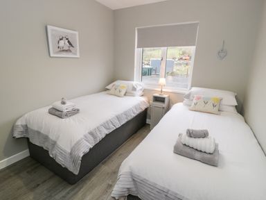 A bedroom with two single beds a nightstand with lamp and window at Cartref in Trawsfynydd