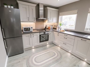 A kitchen with grey cabinets a stainless steel fridge a microwave oven a stovetop a toaster and a rug on the floor at Cartref in Trawsfynydd