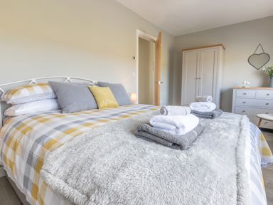 A bedroom with a bed with checkered bedding and folded towels a wardrobe a dresser and a heart-shaped mirror at Cartref in Trawsfynydd