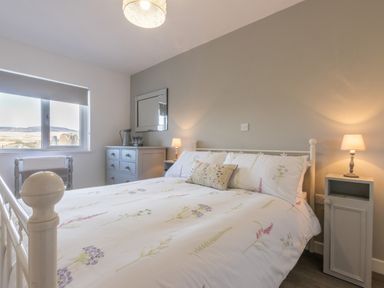 A bedroom with a bed with floral bedding two bedside tables lamps and a chest of drawers under a window at Cartref in Trawsfynydd