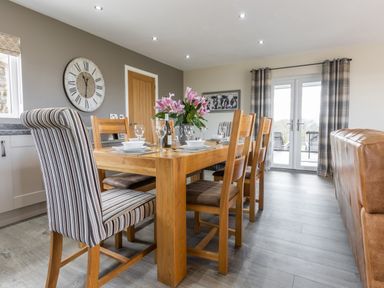 A dining room with wooden table and chairs a striped chair and flowers on the table at Cartref in Trawsfynydd