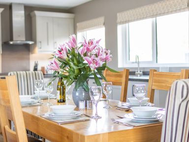 A kitchen dining table set with white dishes glassware and a vase of pink flowers at Cartref in Trawsfynydd