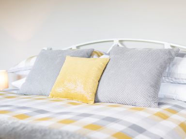 A bed with a checkered duvet and three pillows including two gray and one yellow pillow at Cartref in Trawsfynydd