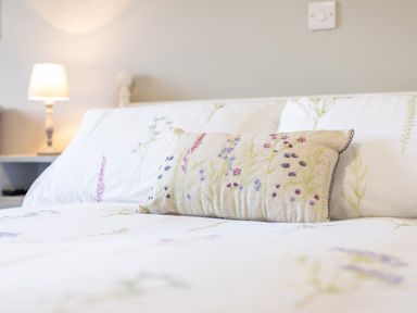 A bed with floral patterned pillows and bedding with a lamp on a bedside table in a bedroom at Cartref in Trawsfynydd