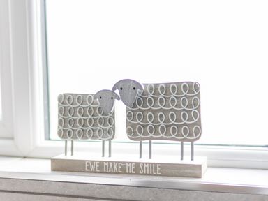 A wooden decoration of two sheep with the text EWE MAKE ME SMILE on a windowsill at Cartref in Trawsfynydd