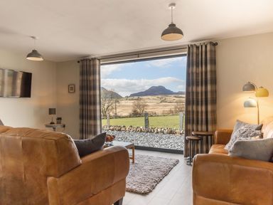 A living room with leather sofas a coffee table and a large window showing countryside at Cartref in Trawsfynydd