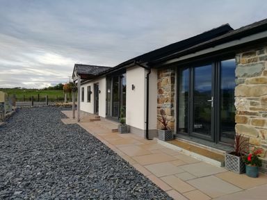 Exterior of a single-story building with stone and white walls doors and windows with plants along a paved path at Cartref in Trawsfynydd