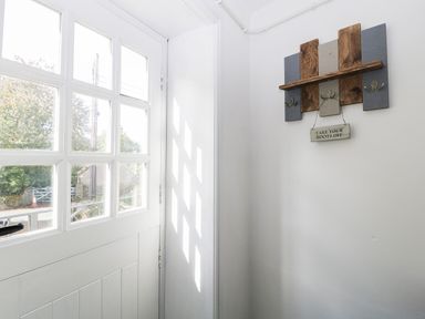 A white door with multiple glass panes and a wooden coat rack with a sign reading take your boots off on a white wall at The Linhay in Chardstock