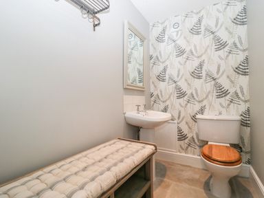 A bathroom with a toilet a sink a wall mirror a bench with cushion and patterned wallpaper at The Linhay in Chardstock