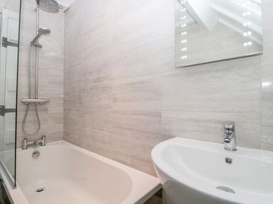 A bathroom with a bathtub shower combination a sink and a mirror on the wall at The Linhay in Chardstock