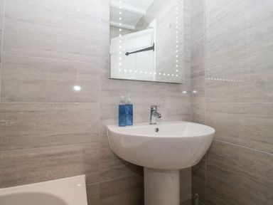 A bathroom corner with a white pedestal sink two blue bottles and a mirror above at The Linhay in Chardstock
