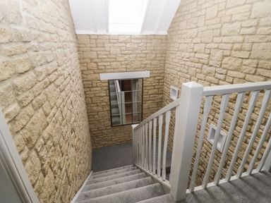 A staircase with grey carpet and white railing with stone walls and a rectangular mirror at The Linhay in Chardstock