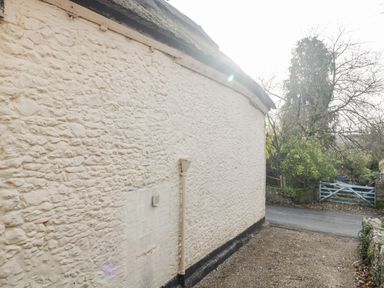 An exterior stone wall of a building with a downpipe and a gravel path leading to a blue wooden gate at The Linhay in Chardstock