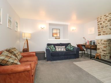 A living room with sofas a floor lamp a desk with a chair and a stone fireplace at The Linhay in Chardstock