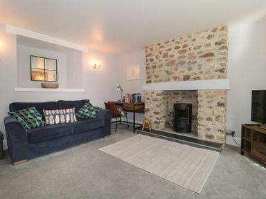 A living room with a blue sofa, stone fireplace, desk with chair, and a rug at The Linhay in Chardstock