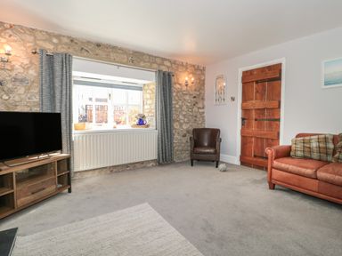 A living room with a stone wall window a brown leather armchair a wooden door a brown sofa and a television at The Linhay in Chardstock