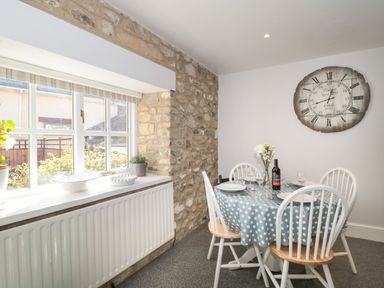 A dining area with a round table and four chairs near a window with stone wall at The Linhay in Chardstock